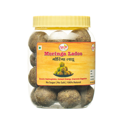 A round, brown Moringa Laadu sweet sits inside a clear plastic jar with a yellow lid. The Amrita label, in English and Hindi, highlights this nutritious snack’s natural ingredients and immunity-boosting benefits.